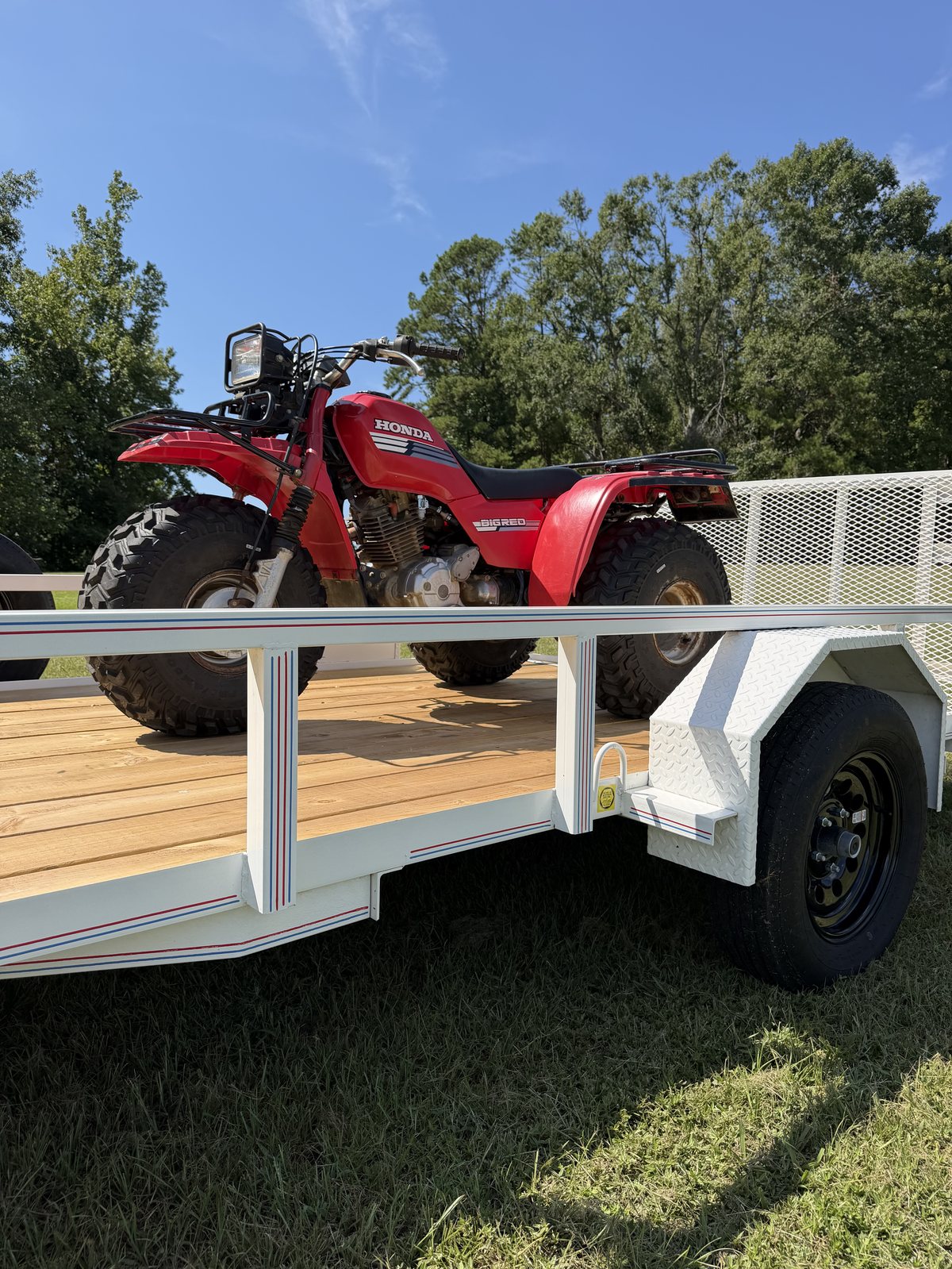 Red Honda ATV loaded on the treated wood deck of a white Triple R utility trailer