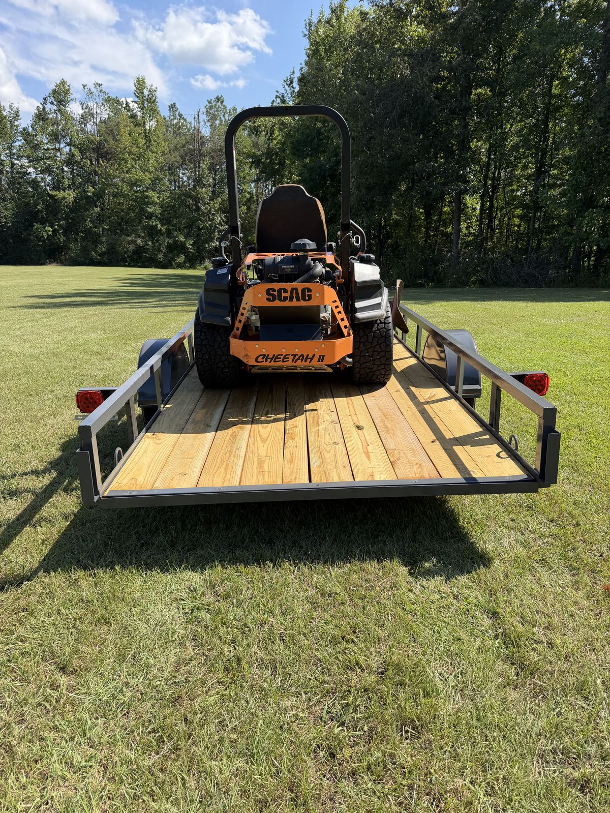 Scag zero turn mower parked on the deck of a Triple R utility trailer with the rear gate down